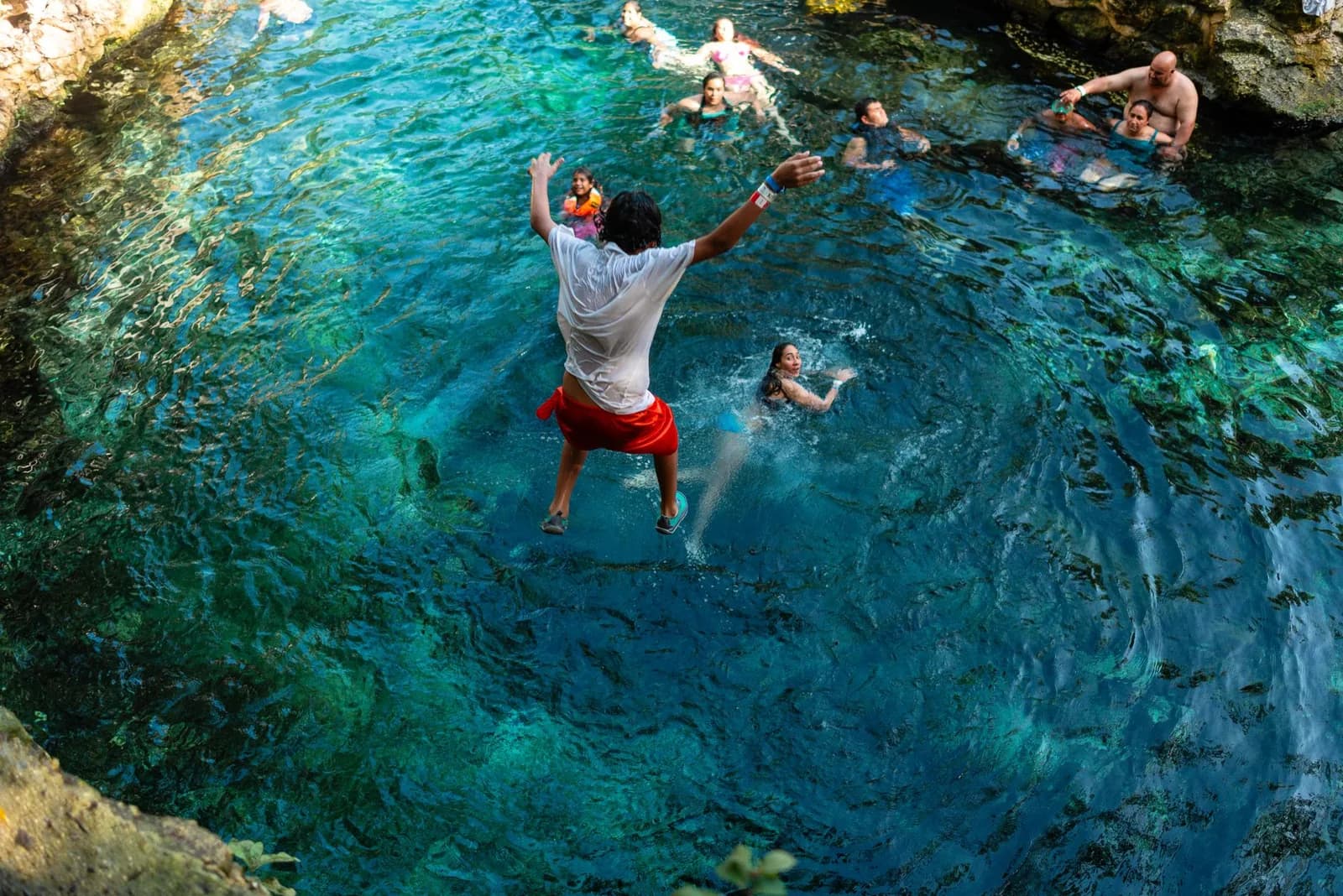 People swimming and jumping into a clear turquoise natural rock pool