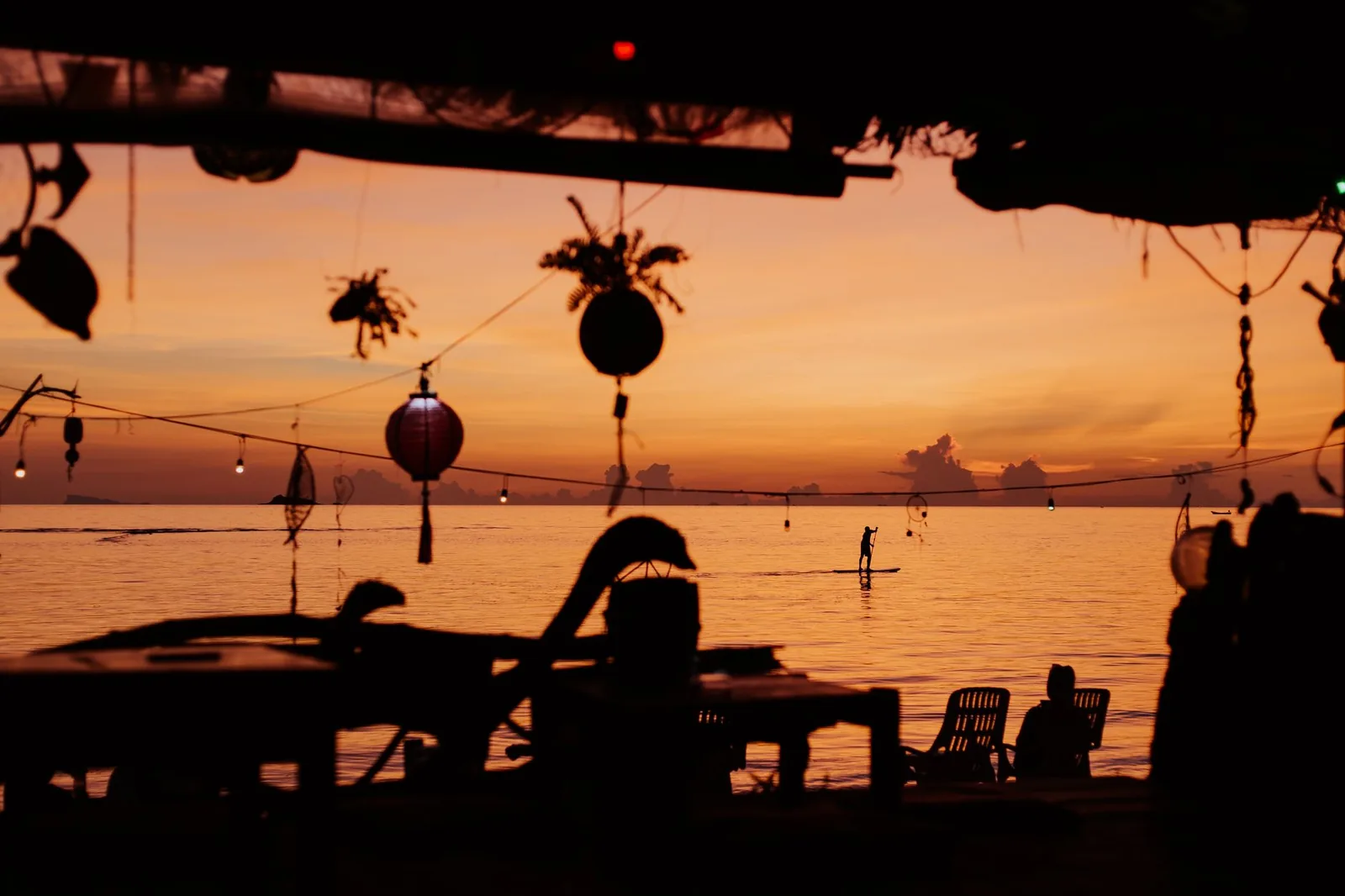 Beach bar silhouetted at sunset with hanging lanterns and string lights over the sea