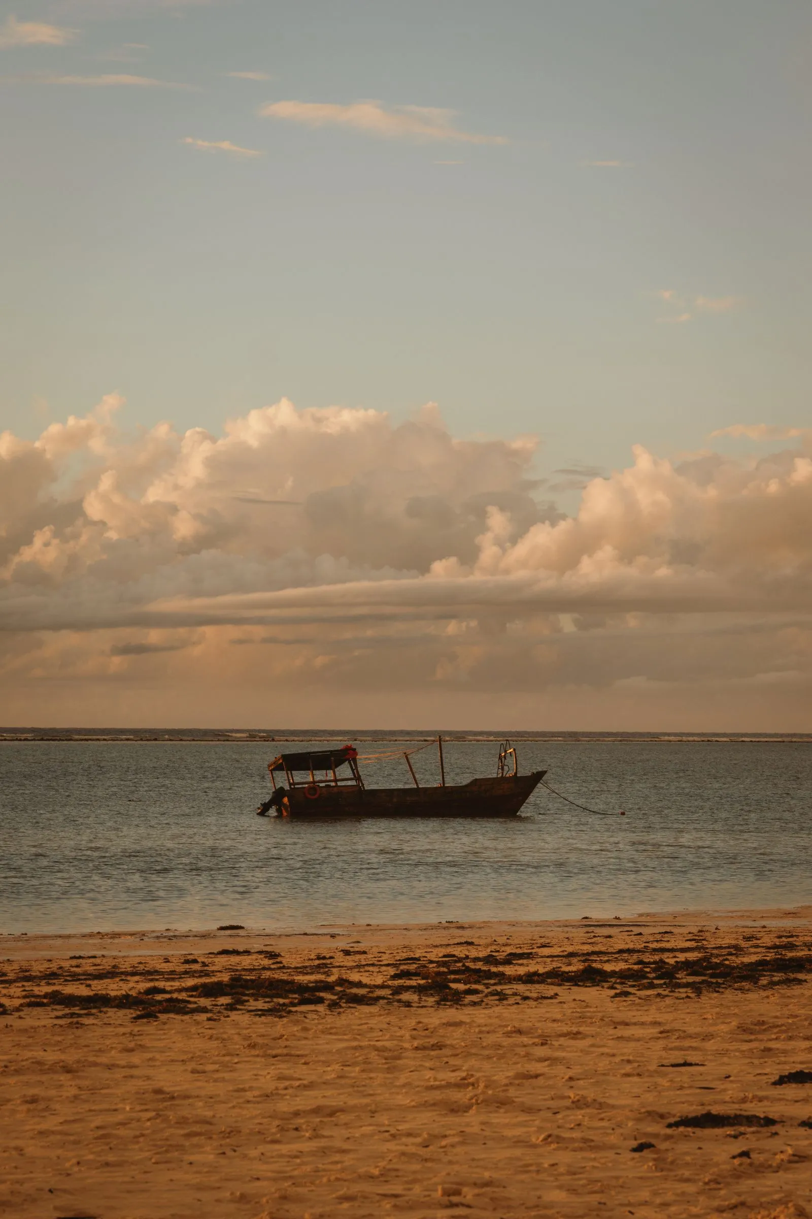 Wooden boat at anchor off a Zanzibar beach at dusk, with the reef breaking on the horizon
