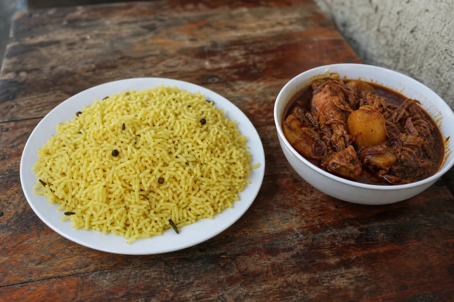 Zanzibar-style biryani with yellow rice served beside a separate bowl of chicken masala with fried onion