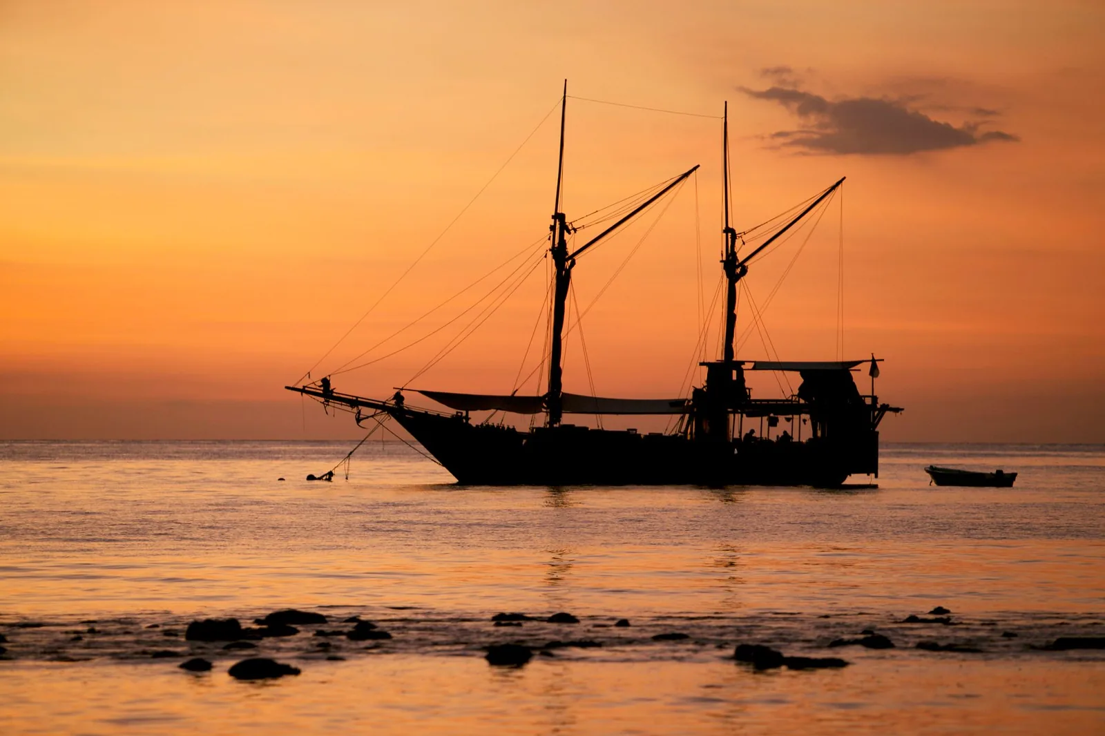 Silhouette of a sailing boat on the shore against an orange tropical sunset