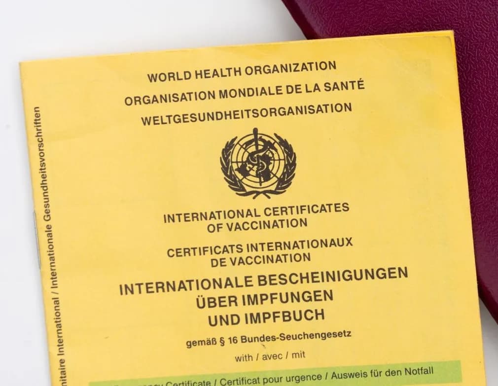 A yellow International Certificate of Vaccination booklet from the World Health Organization, lying on a passport