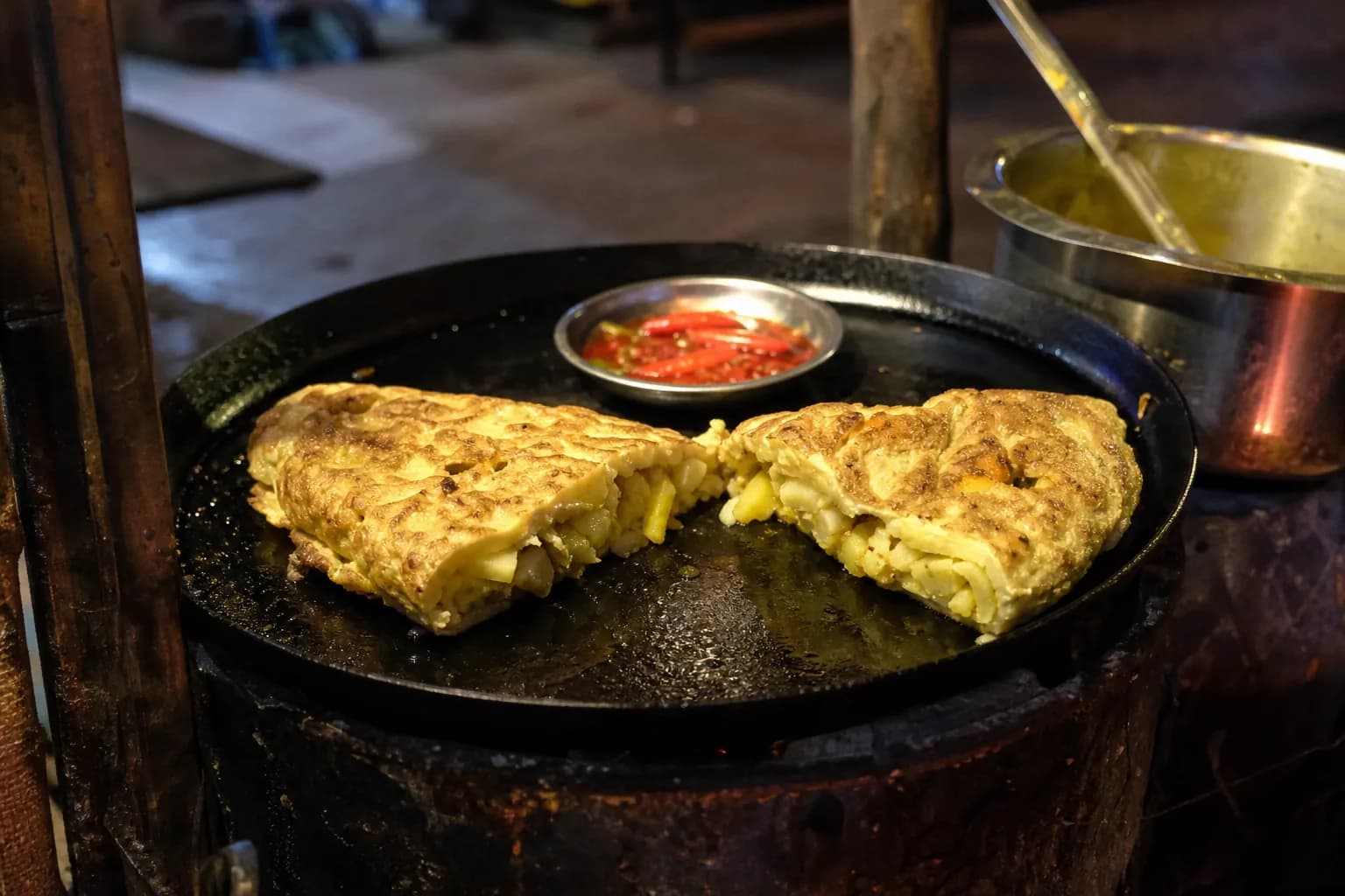 A chipsi mayai chip omelette cut in half on a street griddle with chilli sauce, Zanzibar