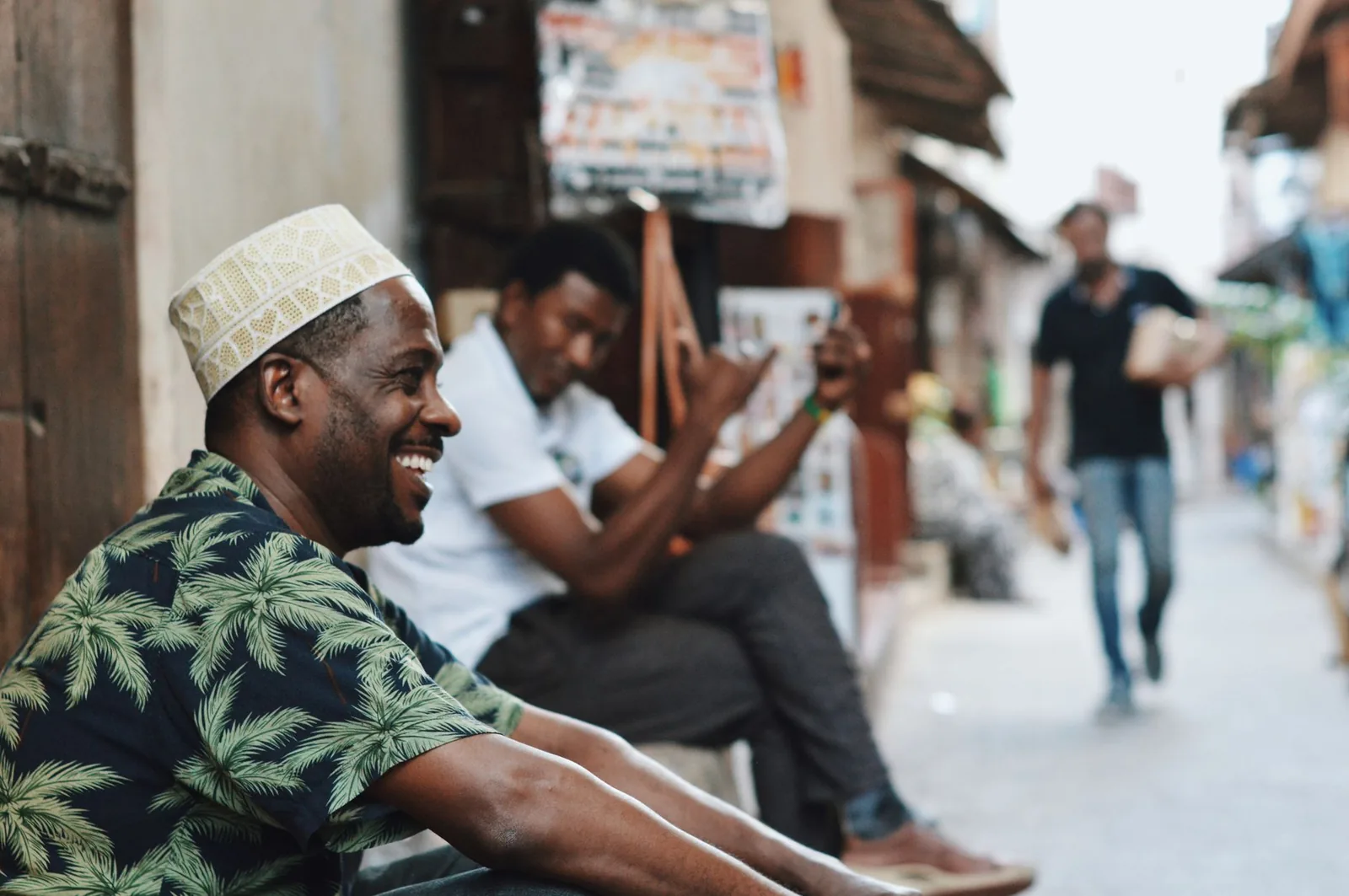 Local men in kofia caps laughing and chatting in a Stone Town alley, Zanzibar