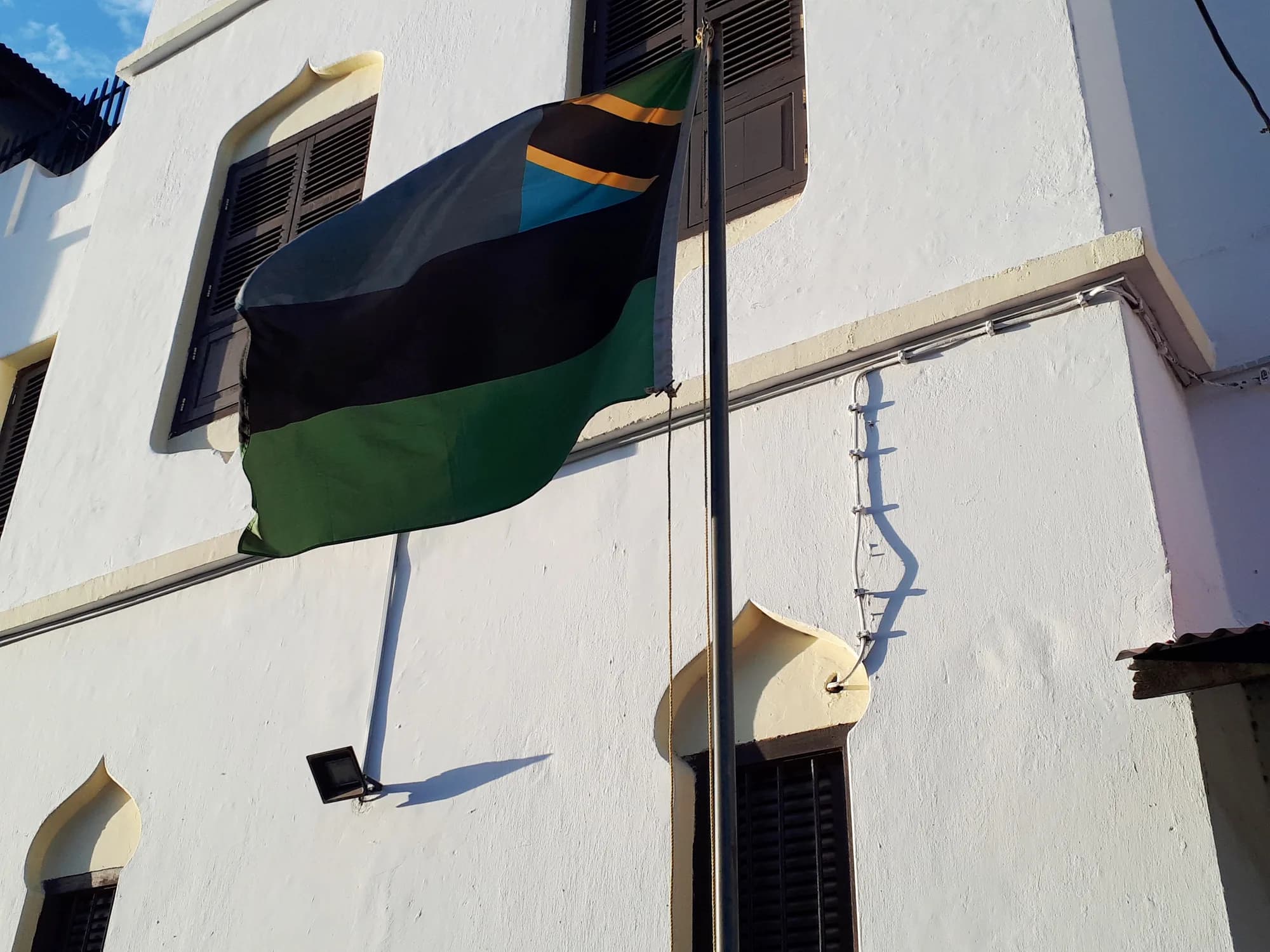 The Zanzibar flag, blue, black and green with the Tanzanian canton, flying against a whitewashed building in Stone Town