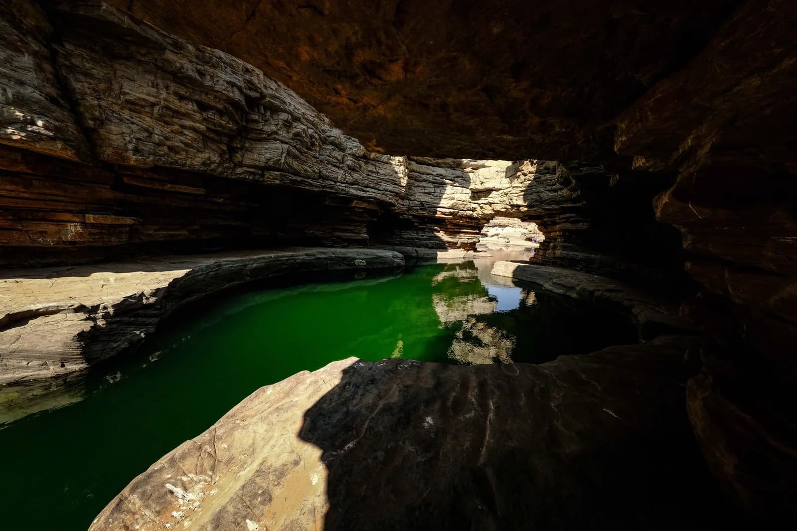 Green water pool inside a layered limestone cave