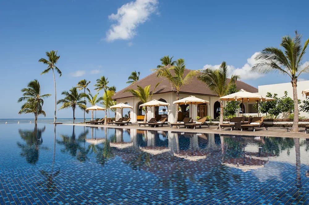 Infinity pool and thatched-roof lounge pavilion with sun loungers and palm trees at The Residence Zanzibar, Kizimkazi