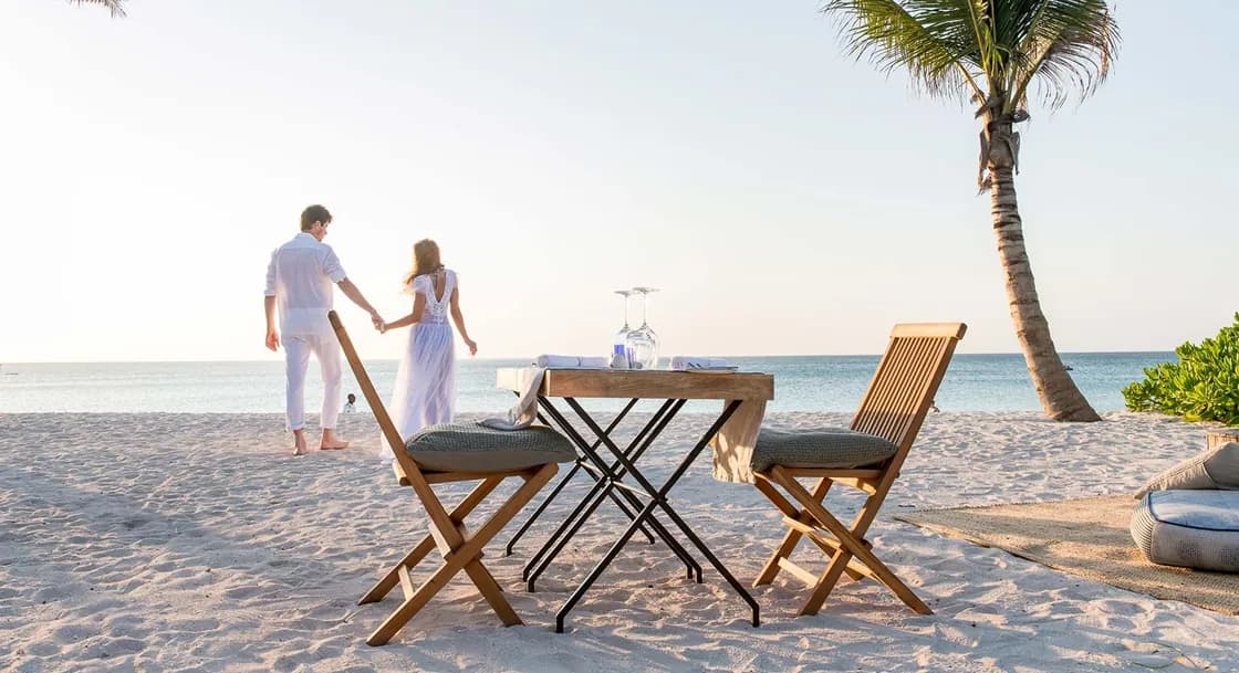 A couple walking towards the sea past a table set on the white sand beach at Zuri Zanzibar, Kendwa