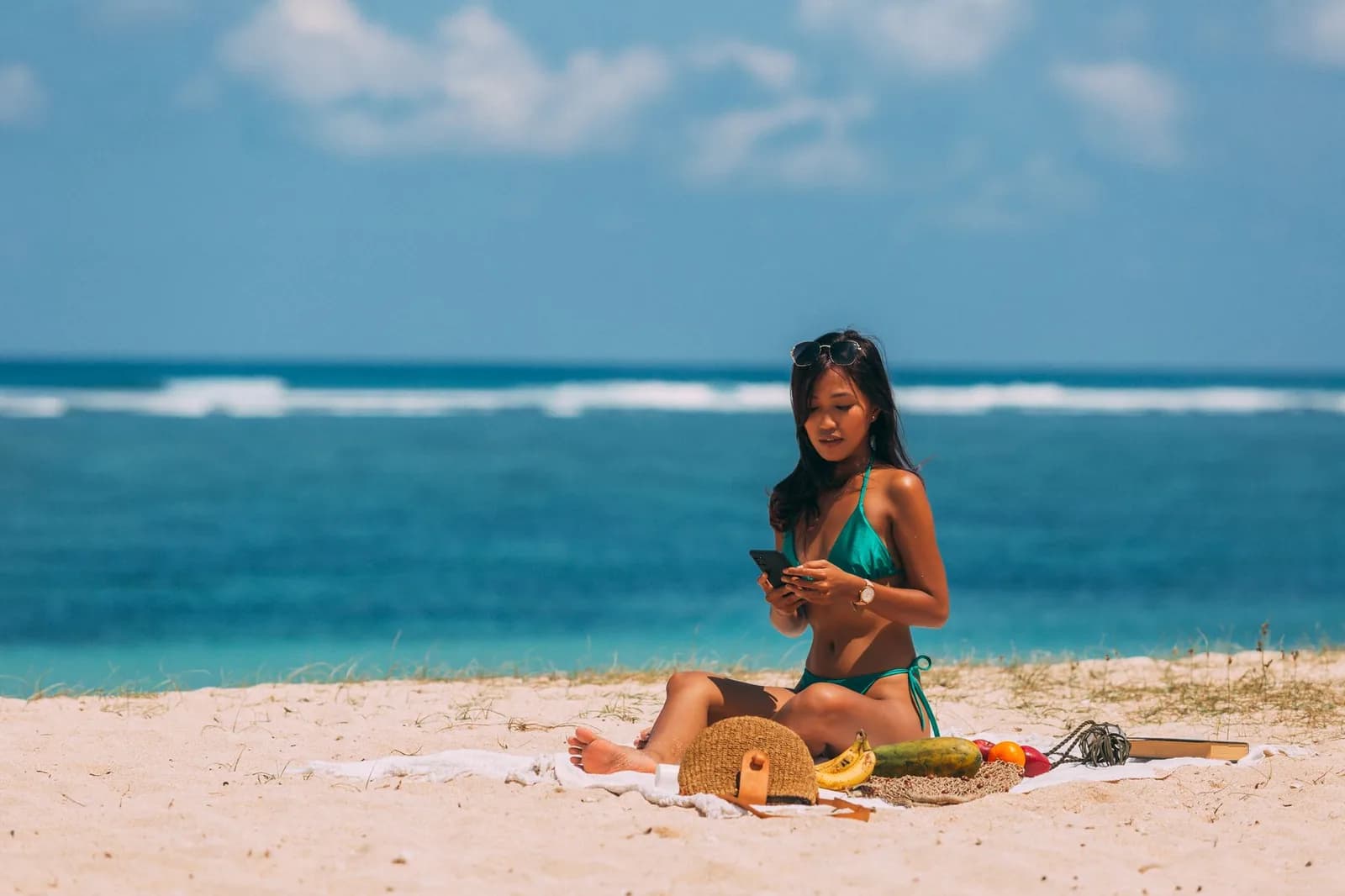 Someone sitting on the sand checking a phone, with the reef breaking offshore