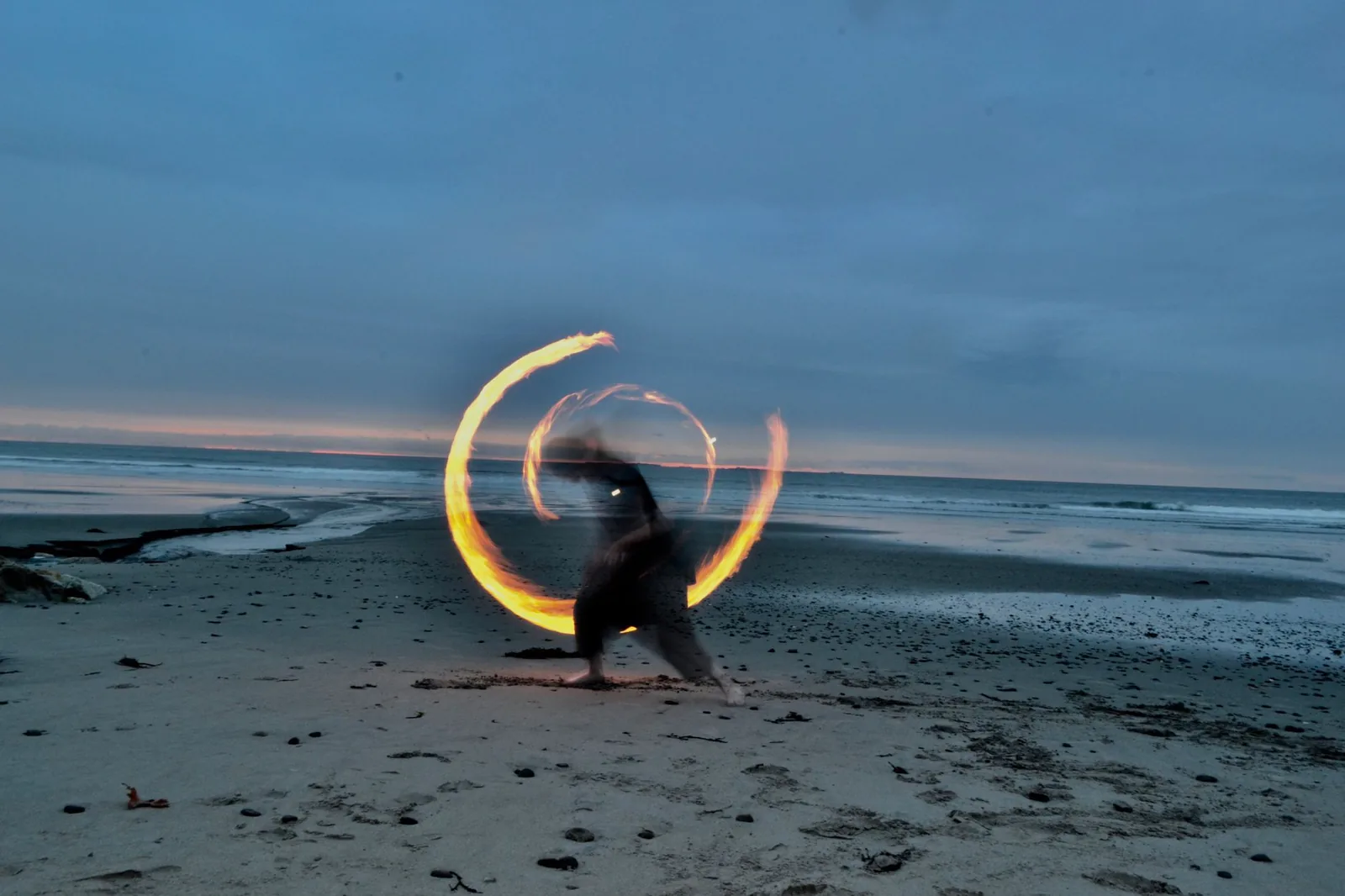 Fire performer spinning a glowing ring of light on a beach at dusk