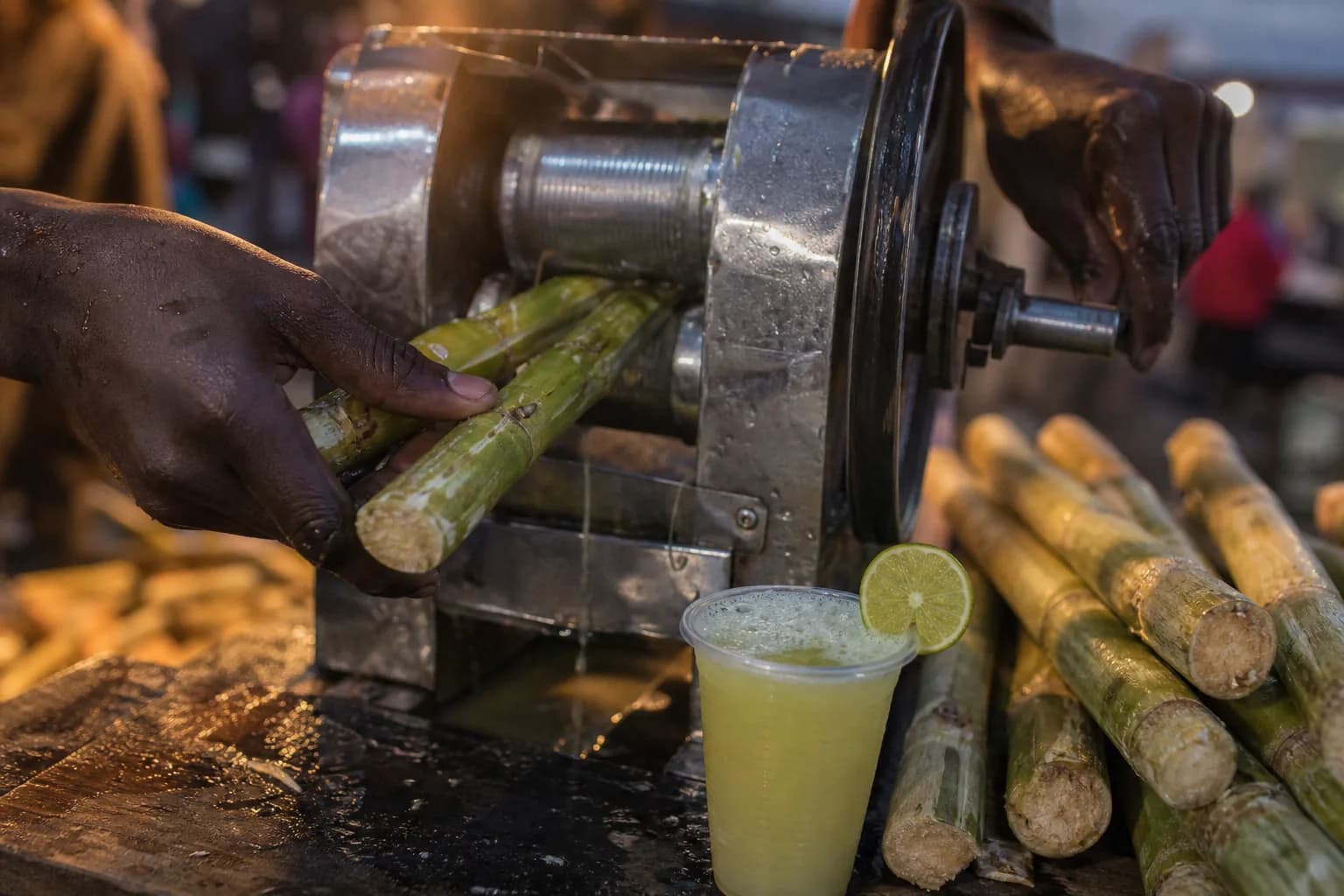 Sugar cane fed through a hand-cranked press at an evening market in Zanzibar, with a cup of juice and lime