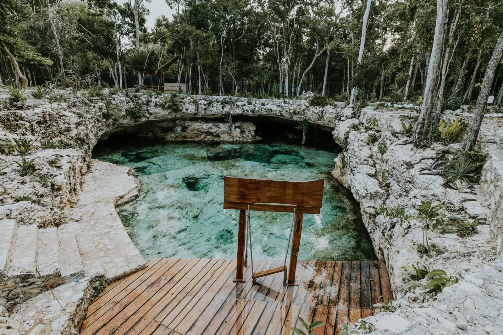 Clear turquoise cave pool in white limestone with a wooden viewing platform and stone steps