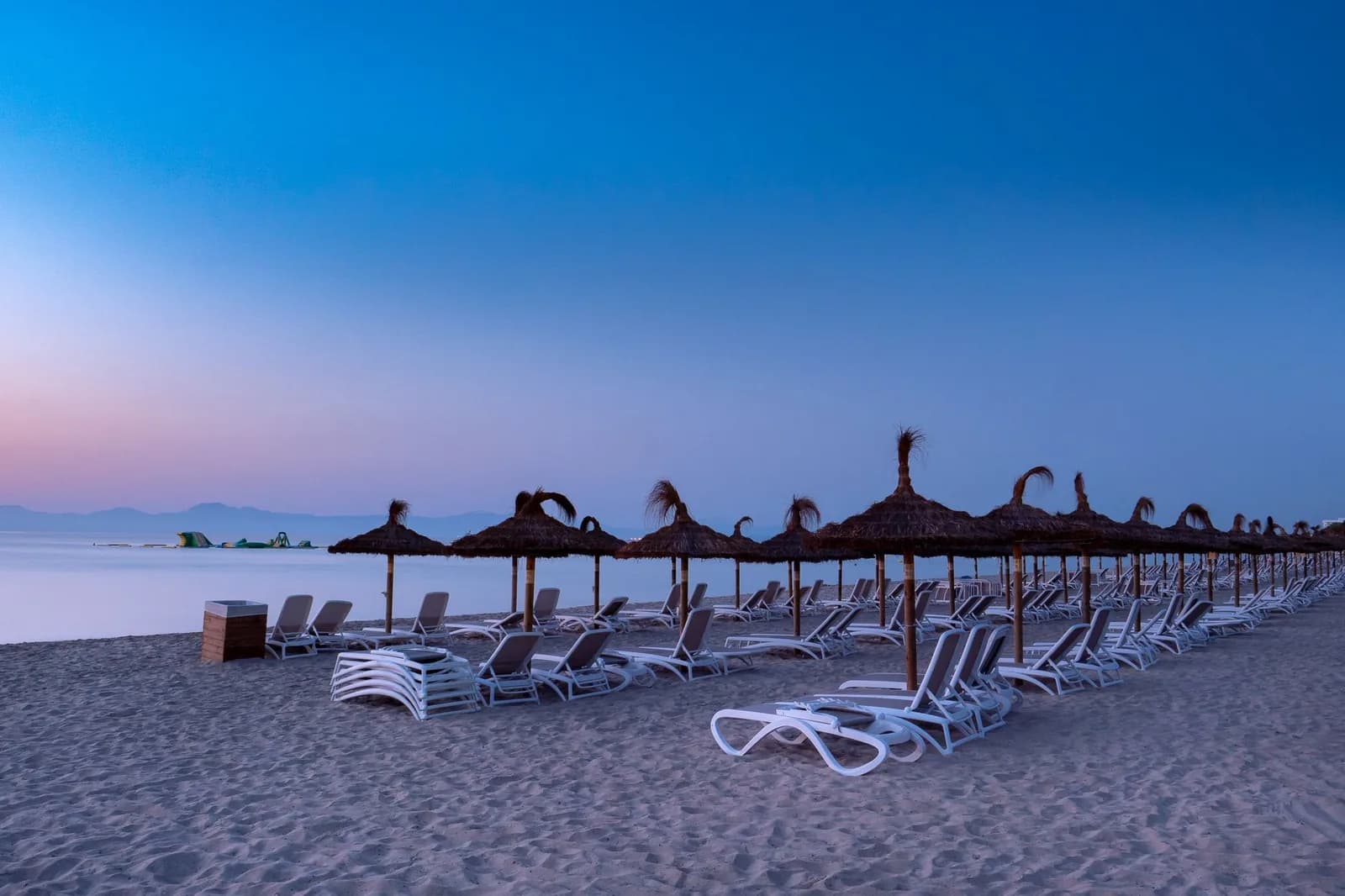 Row of empty sun loungers and thatched parasols on a quiet beach at dusk