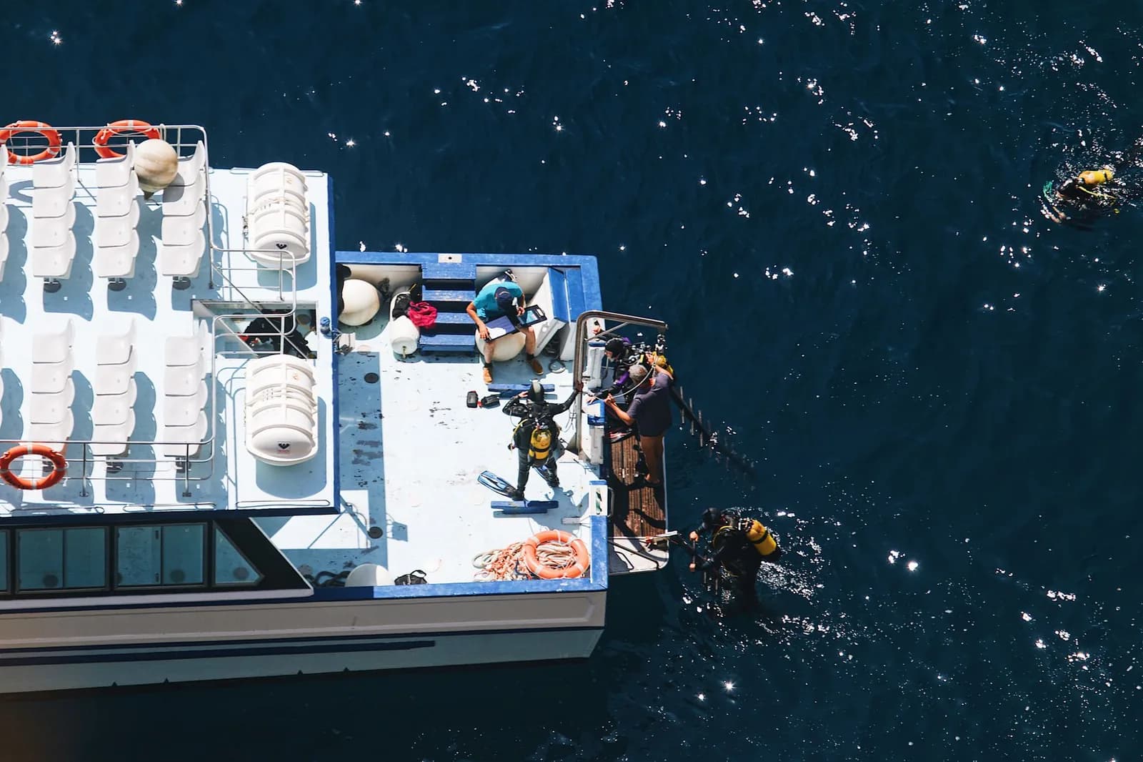 Divers entering the water from the stern of a dive boat, seen from directly above