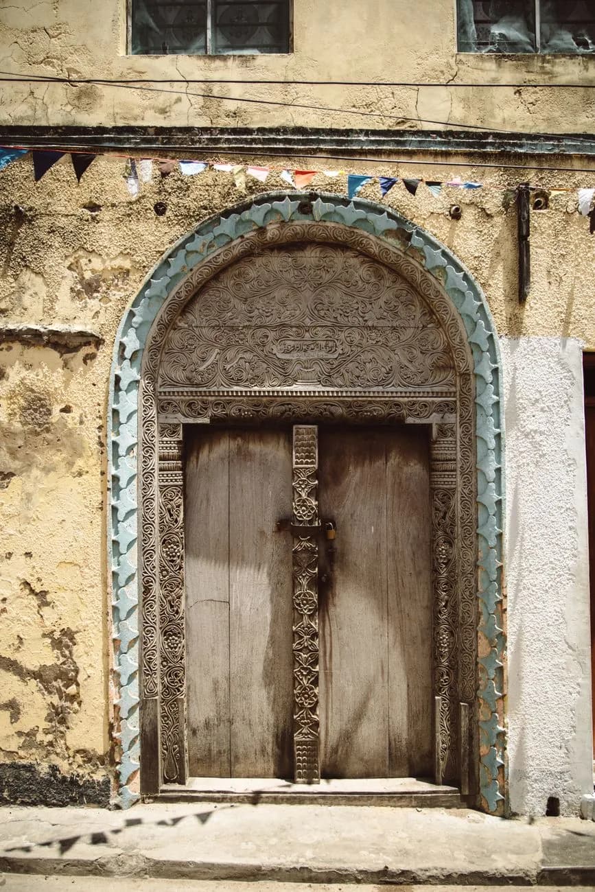 A carved wooden door under a painted arch in Stone Town, Zanzibar