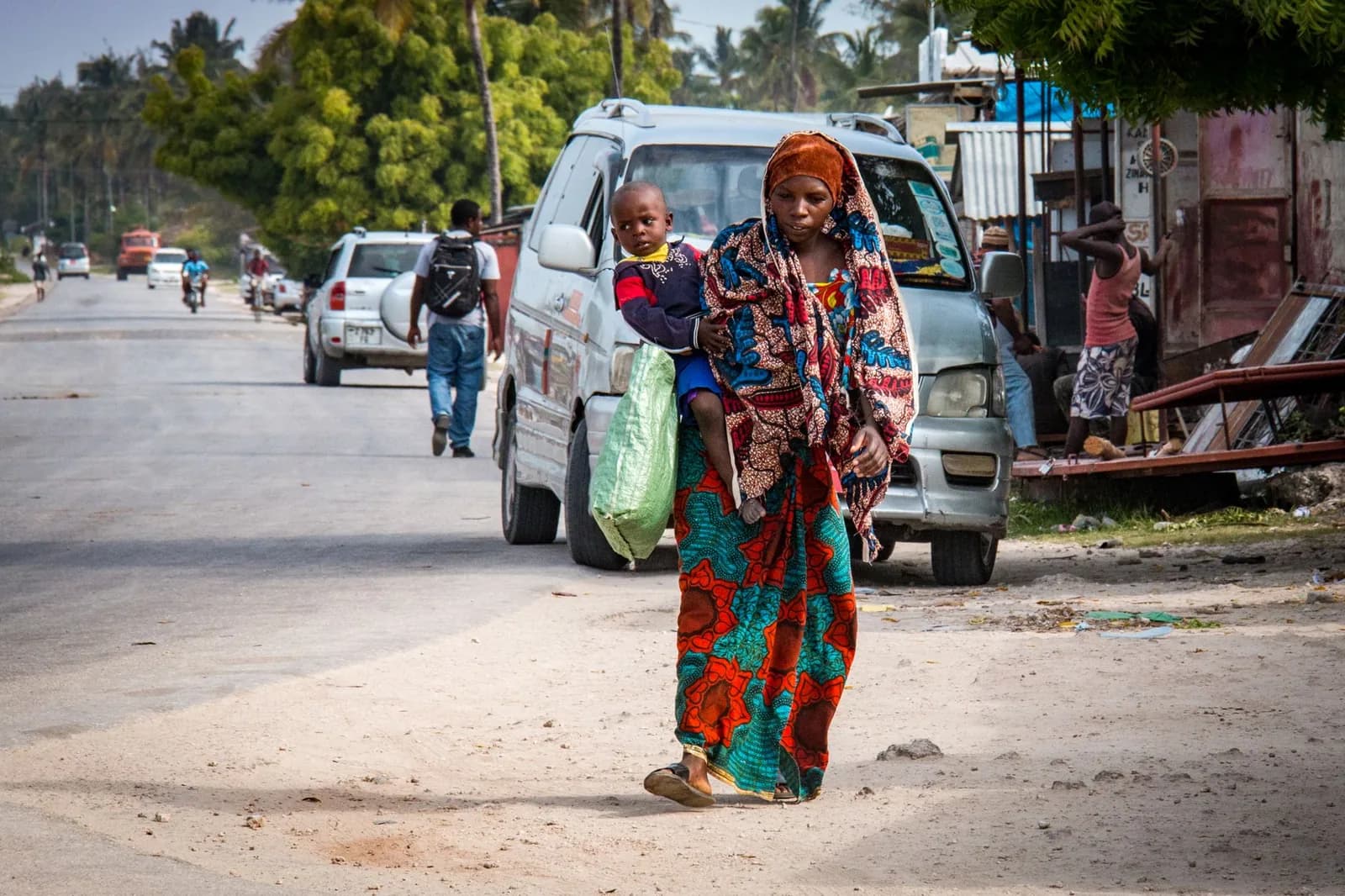 A village main road in Zanzibar, with parked 4x4s and a sandy verge