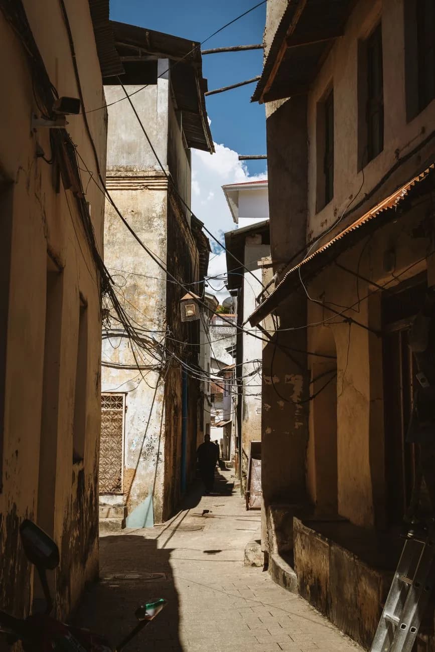 A narrow shaded lane between old coral stone buildings in Stone Town, Zanzibar, with electric cables overhead