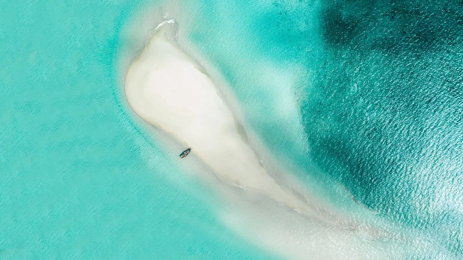 A boat moored against a white sandbank surrounded by turquoise shallows in Menai Bay