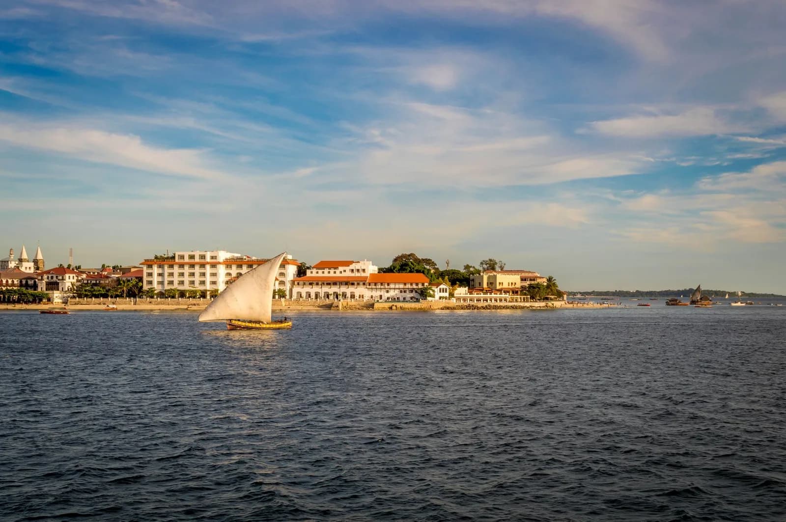 A dhow under sail in front of the Stone Town seafront, Zanzibar, in the late afternoon light