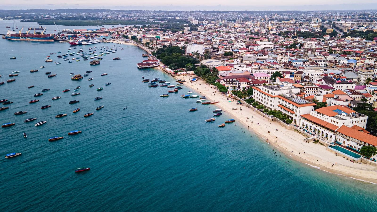 Aerial view of the Stone Town seafront in Zanzibar, with boats at anchor, the beach and the port beyond