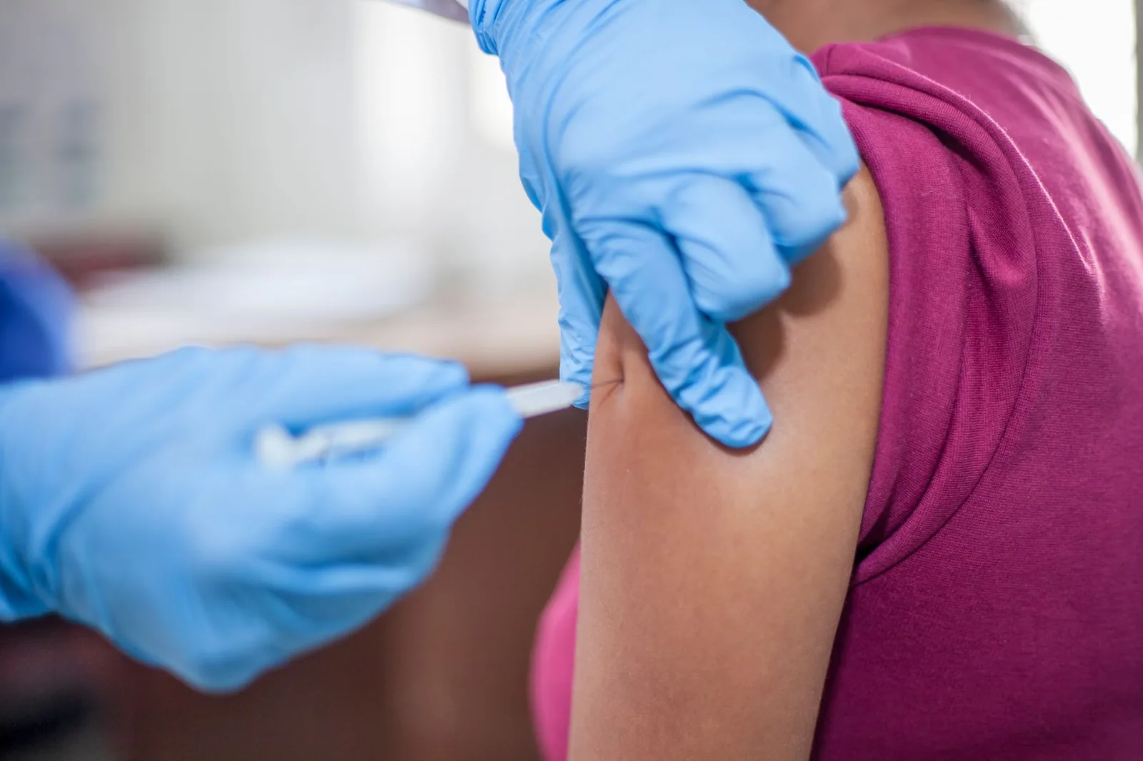 A health worker in blue gloves giving a vaccination injection in a patient's upper arm